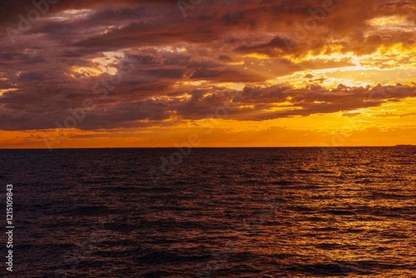 Fototapeta the water surface of the sea under a cloudy sky, illuminated by the rays of the setting sun at sunset