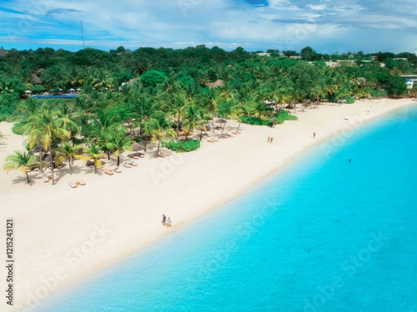 Fototapeta Aerial view of empty white sandy beach with palms, umbrellas, blue ocean, sky with clouds at sunset. Summer in Kendwa, Zanzibar island. Tropical landscape. Clear sea with azure water. Top view