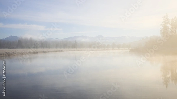 Fototapeta Background warm morning light spreads across foggy blue lake with distant trees and mountains