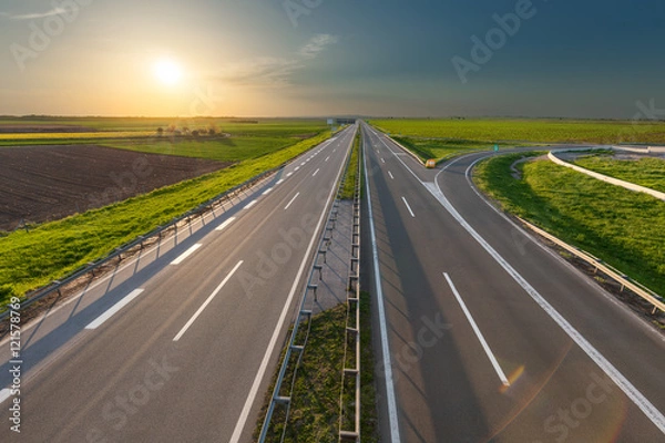 Fototapeta Open freeway through illuminated green idyllic fields