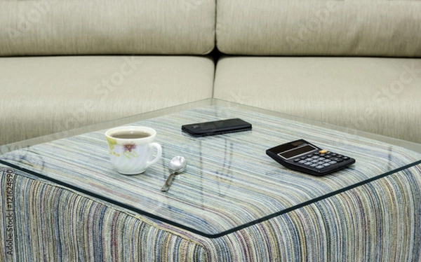 Obraz Cup of coffee, mobile phone and calculator on glass table. Simple workspace or coffee break in morning