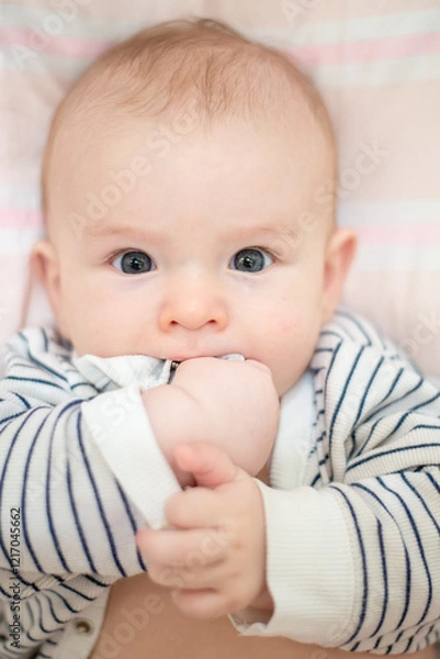 Fototapeta child beautiful happy boy with black eyes holds hands in mouth, close-up