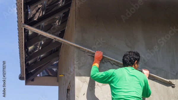 Obraz Plastering the cement wall of an outdoor house building with workers working on a construction site