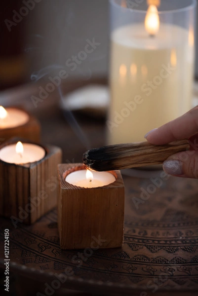 Fototapeta A stick of palo santo incense in a woman's hand smolders against the background of candles