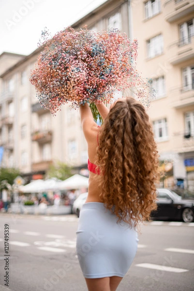 Fototapeta Colorful flowers in voluminous bouquet in a hands of a girl who goes on a street