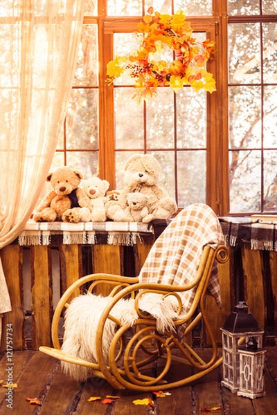 Fototapeta rocking-chair in the room with wooden walls, wicker wreath in autumn style hanging on the window