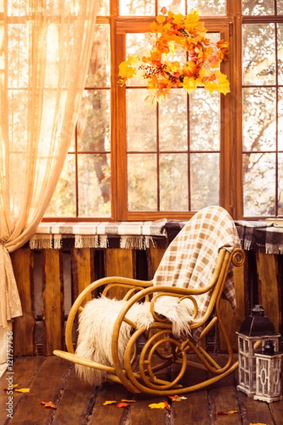 Fototapeta rocking-chair in the room with wooden walls, wicker wreath in autumn style hanging on the window