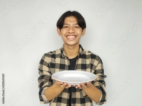 Fototapeta Young Asian man smiling happily while pointing at empty dinner plate
