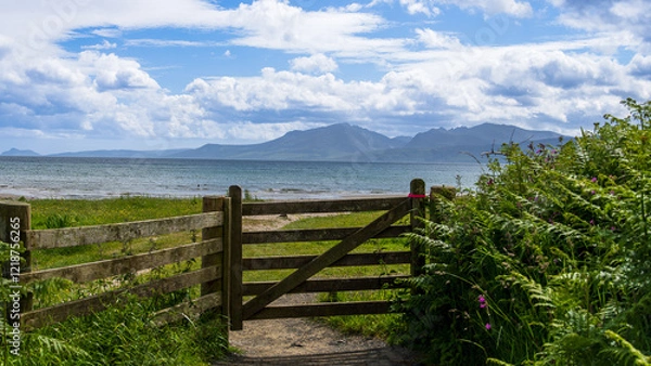Fototapeta Scotland, Isle of Bute. Photo taken on: 08-06-2024. A serene coastal scene with a wooden gate, greenery, and mountains in the background.