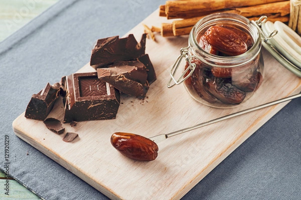 Fototapeta Chocolate, date fruit and cinnamon on a white chopping board on a blue table. Pastel colors