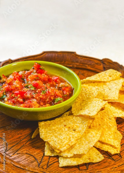 Fototapeta Vertical view fresh homemade salsa made with organic tomatoes and basil in a vintage bowl and organic corn chips on an antique wooden tray with copy space.