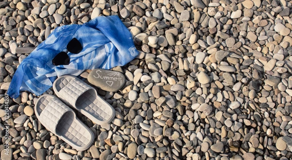 Obraz Black sunglasses, pareos and flip-flops on a pebble beach on a warm sunny day. The concept of summer holidays.