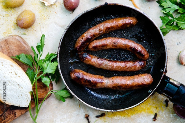 Fototapeta Grilled sausages, merguez in a frying pan, with olives, baguette and spices, top view