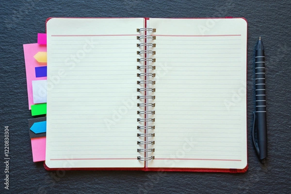 Fototapeta Open spiral bound notebook with blank pages and colorful bookmarks. Dark background, flat lay, copy space