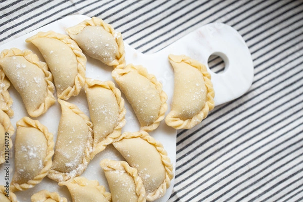 Fototapeta Fresh homemade dumplings prepared on a marble board, showcasing traditional handmade craftsmanship. Raw dough filled with savory ingredients, ready for cooking.