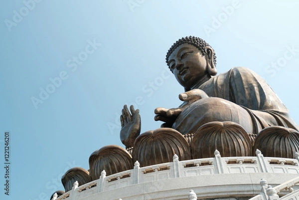 Fototapeta Majestic Bronze Buddha Statue with Hand Gesture Against a Clear Blue Sky