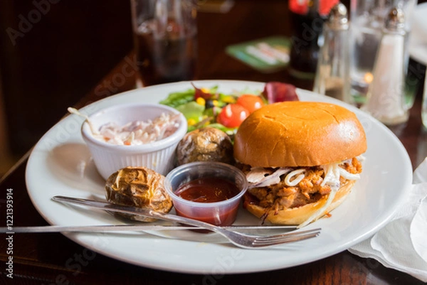 Fototapeta Traditional Irish pub pulled pork burger. Grilled pulled pork burger on a plate with potatoes and salad