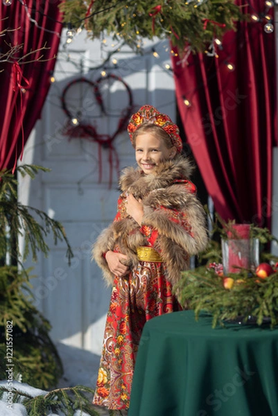 Fototapeta A blonde girl in a national Russian costume on the Maslenitsa holiday. A child in a traditional costume with fur trim and a headdress against a festive backdrop. Winter scene with a beautiful girl