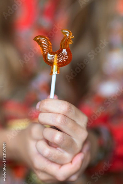 Fototapeta Lollipop shaped like a cockerel. An element of Russian folklore.A child's hands hold a lollipop in close-up