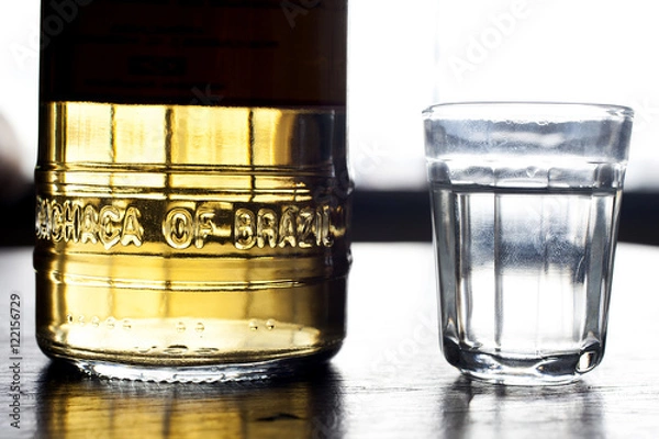 Fototapeta A bottle and a shot of cachaca on rustic background with natural light.