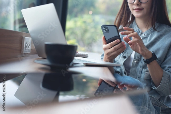 Obraz Young asian business woman using mobile phone and working on laptop computer at coffee shop. Woman freelancer online working, surfing the internet at cafe, business casual