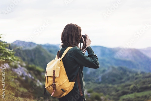 Fototapeta Tourist traveler photographer taking pictures landscape on vintage photo camera on background valley view mockup sun flare, hipster girl with backpack enjoying sunset on peak of foggy mountain