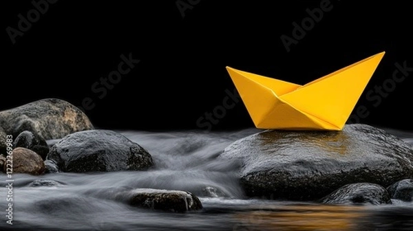 Fototapeta Yellow Origami Boat Floating on Smooth Water Over Dark Rocks Creating a Tranquil Scene