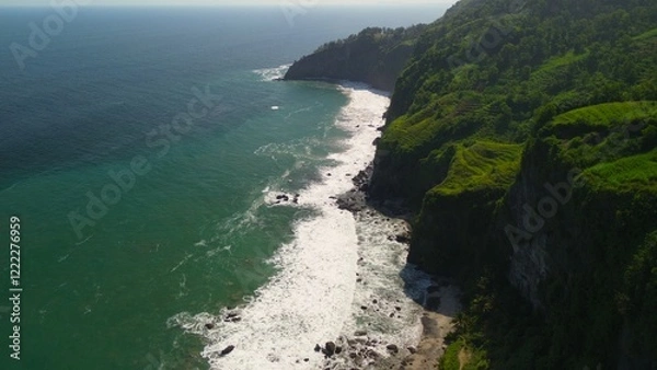 Fototapeta  A man standing in the top of hill in coastline with hills, cliffs, trees, beach sand and waves from the sea and ocean at Menganti Beach, Kebumen, Central Java, Indonesia
