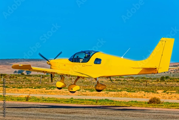 Obraz Bright yellow two-seater low-wing light-sport aircraft taking off from a small airfield in the Western Cape, South Africa