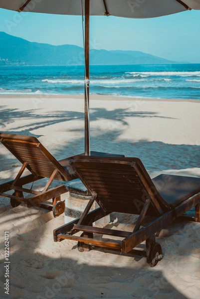 Fototapeta Relaxing beach scene with empty lounge chairs under umbrella on sandy shore