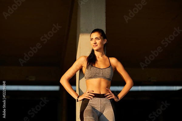 Fototapeta Portrait of a tired but satisfied with her training woman runner resting after workout while looking at the sun