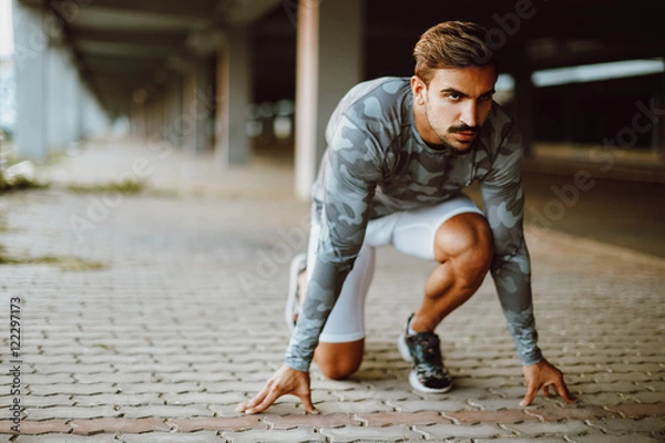 Fototapeta Fit and confident man in starting position ready for running. Male athlete about to start a sprint