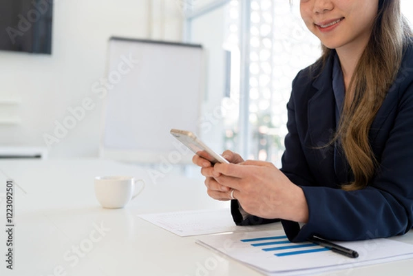 Obraz Businesswoman sitting at desk on couch in workplace or at home working on laptop and analyzing data on charts and graphs and writing on papers to make business plan and strategies for company.