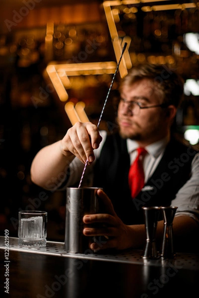 Fototapeta Bartender stirs a cocktail in a tall metal glass with a long bar spoon