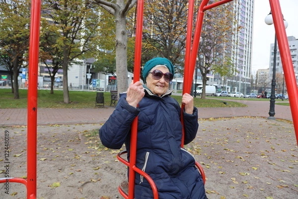 Fototapeta Senior lady enjoying ride on swings in park, retirement