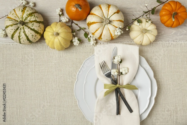 Fototapeta Fall autumn festive table setting place setting with pumpkins, plate, fork, knife and napkin on burlap background