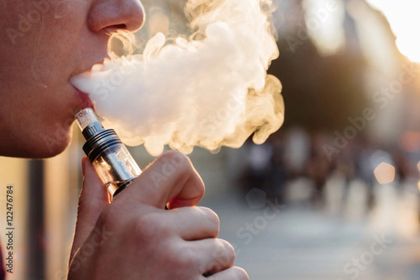 Obraz man using vape or electronic cigarette against the background of