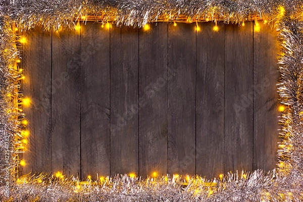 Fototapeta Christmas lights on a wooden background with free space. Frame with silver christmas chain.