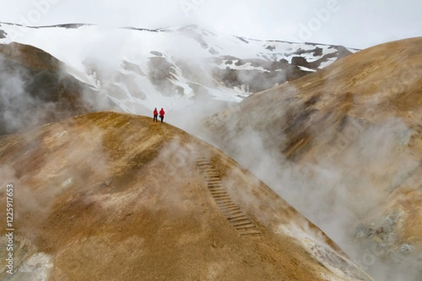 Obraz Scenic aerial drone view of a couple hikers in red jackets and foggy Kerlingarfjoll mountain path amidst desert and snowy terrain in Iceland