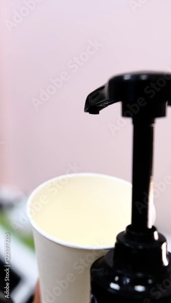 Fototapeta Barista adds red cherry syrup to a white paper coffee cup using a dispenser at coffee shop creating delicious flavored drink with vibrant color perfect for coffee lovers seeking refreshing beverages