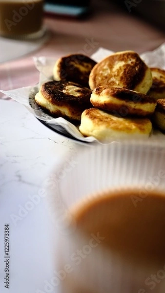 Fototapeta A woman forks fluffy golden pancakes with crispy edges while coffee is in the background out of focus breakfast concept morning meal with pancakes coffee and fork casual dining brunch at home