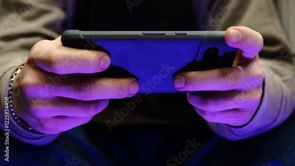 Fototapeta Young man playing mobile game with fast finger movements and colorful pulsating hand lights, dynamic gameplay, close up phone screen, digital entertainment, gaming action, energetic gaming session.