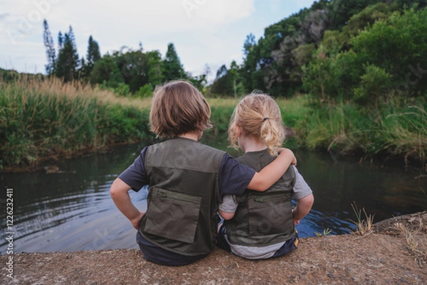 Obraz Two siblings in adventuring clothing hugging each other in front of water