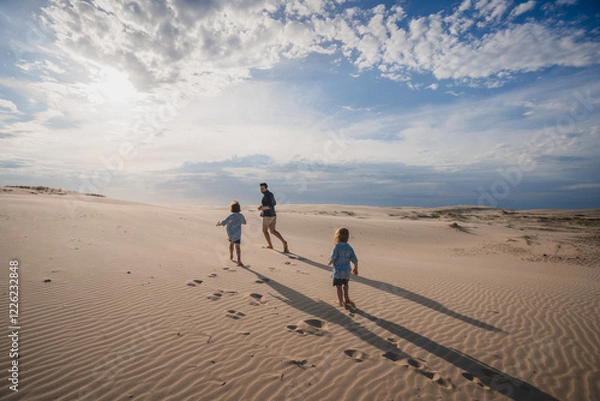 Obraz Two children chasing father on sand dune