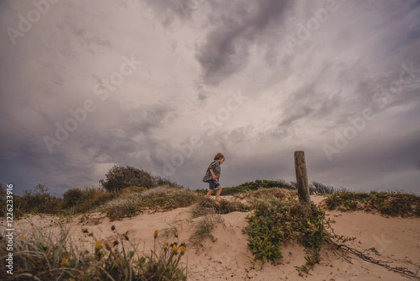 Obraz Boy exploring top of sand dune dramatic sky