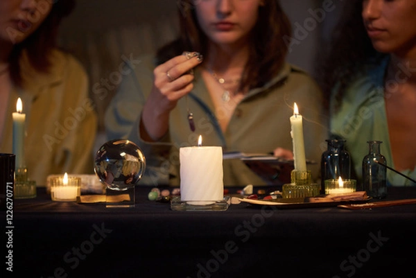 Fototapeta Medium closeup of three diverse female friends practicing divination, while sitting at coffee table with candles and magical objects on it