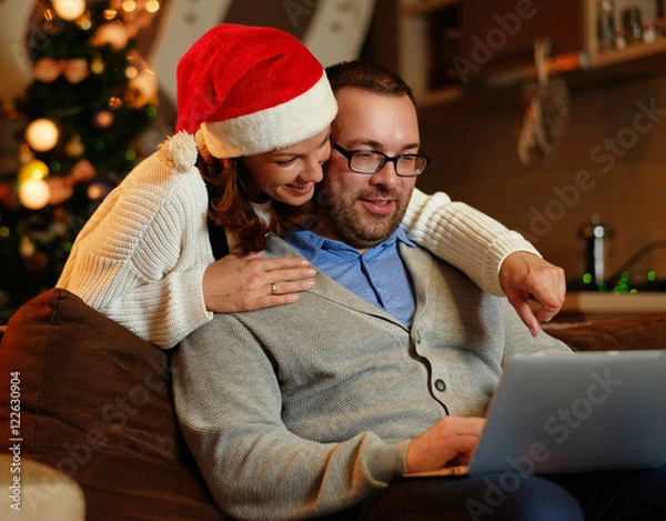Obraz Smiling female and plump male using laptop on christmas.