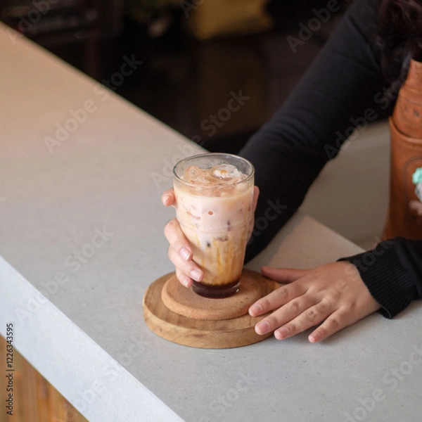 Fototapeta A person enjoys a creamy iced beverage at a stylish cafe, showcasing a blend of textures and flavors on a warm afternoon