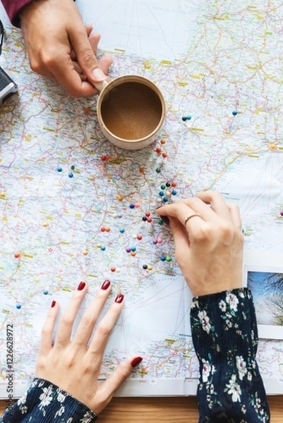 Obraz Hands on a map with colorful pins, planning a journey. Map and pins show travel ideas. Coffee cup nearby. Map, pins, and travel planning scene. Women planning a trip on a map.
