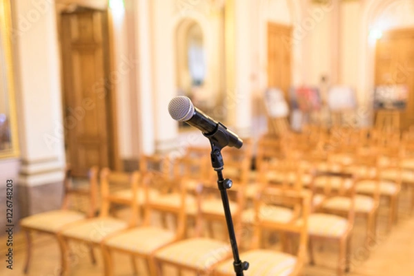 Fototapeta Microphone on a stand in an elegant event hall with empty chairs in soft focus